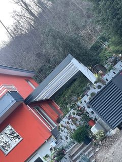 Una casa rossa si erge accanto a un moderno patio coperto con fioriere in pietra, incastonata nel fianco di una collina boscosa.