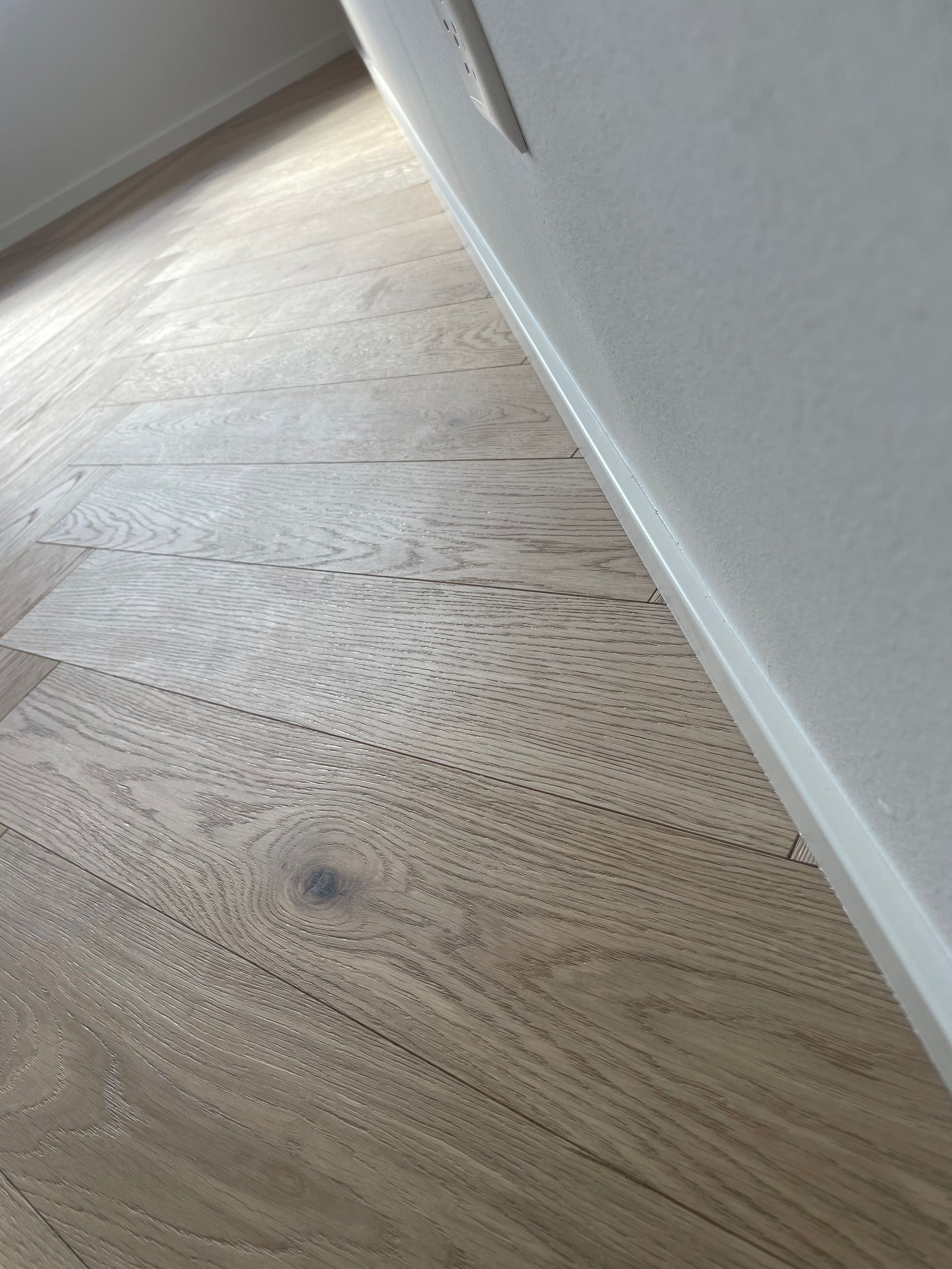 In una stanza, il pavimento in legno a listoni larghi di colore chiaro incontra il battiscopa bianco.