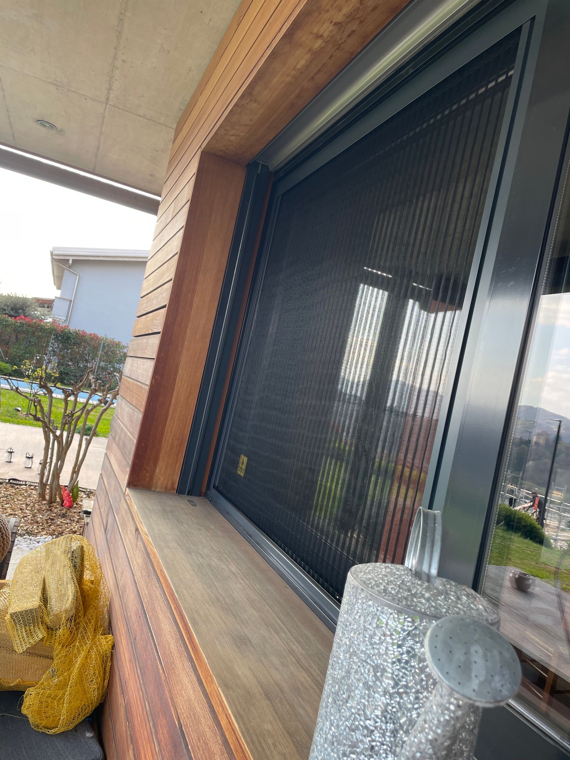 Una porta a zanzariera in metallo nero installata all'esterno di un'abitazione con rivestimento in legno e davanzale in pietra.