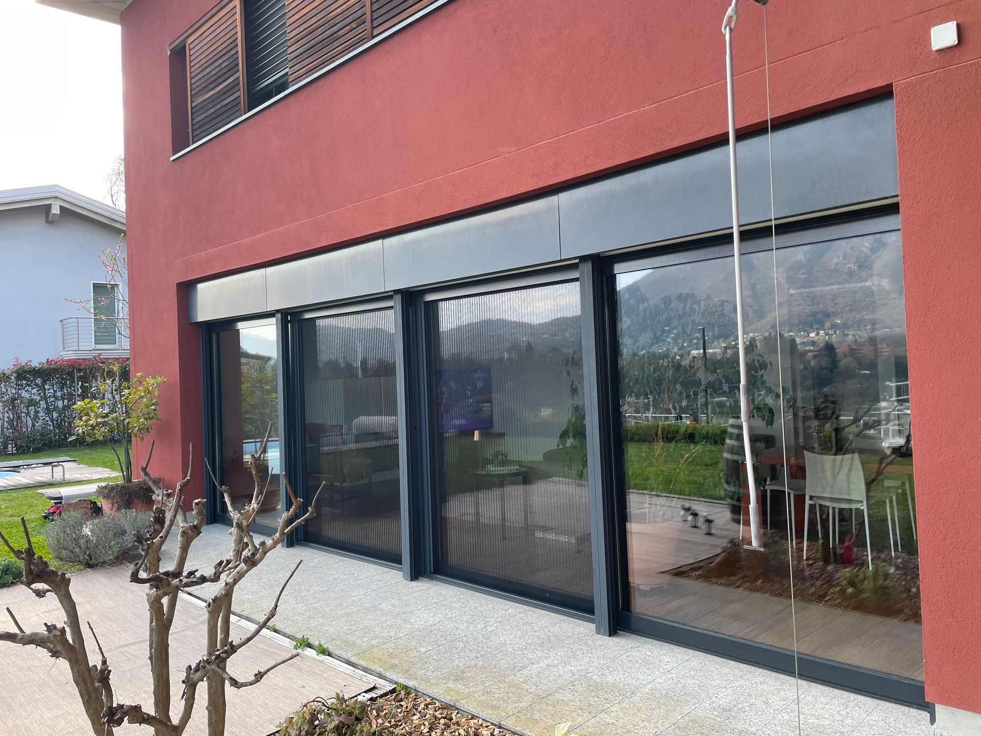 Un edificio residenziale rosso con grandi porte scorrevoli in vetro con cornici scure che si aprono su un patio e un cortile erboso.