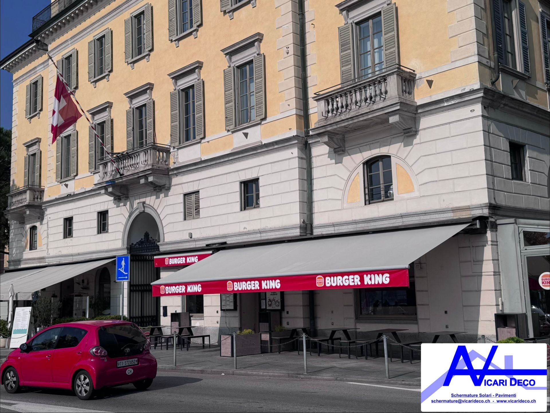 Un ristorante Burger King con tende rosse situato al piano terra di un edificio storico a più piani, dalle tonalità gialle.