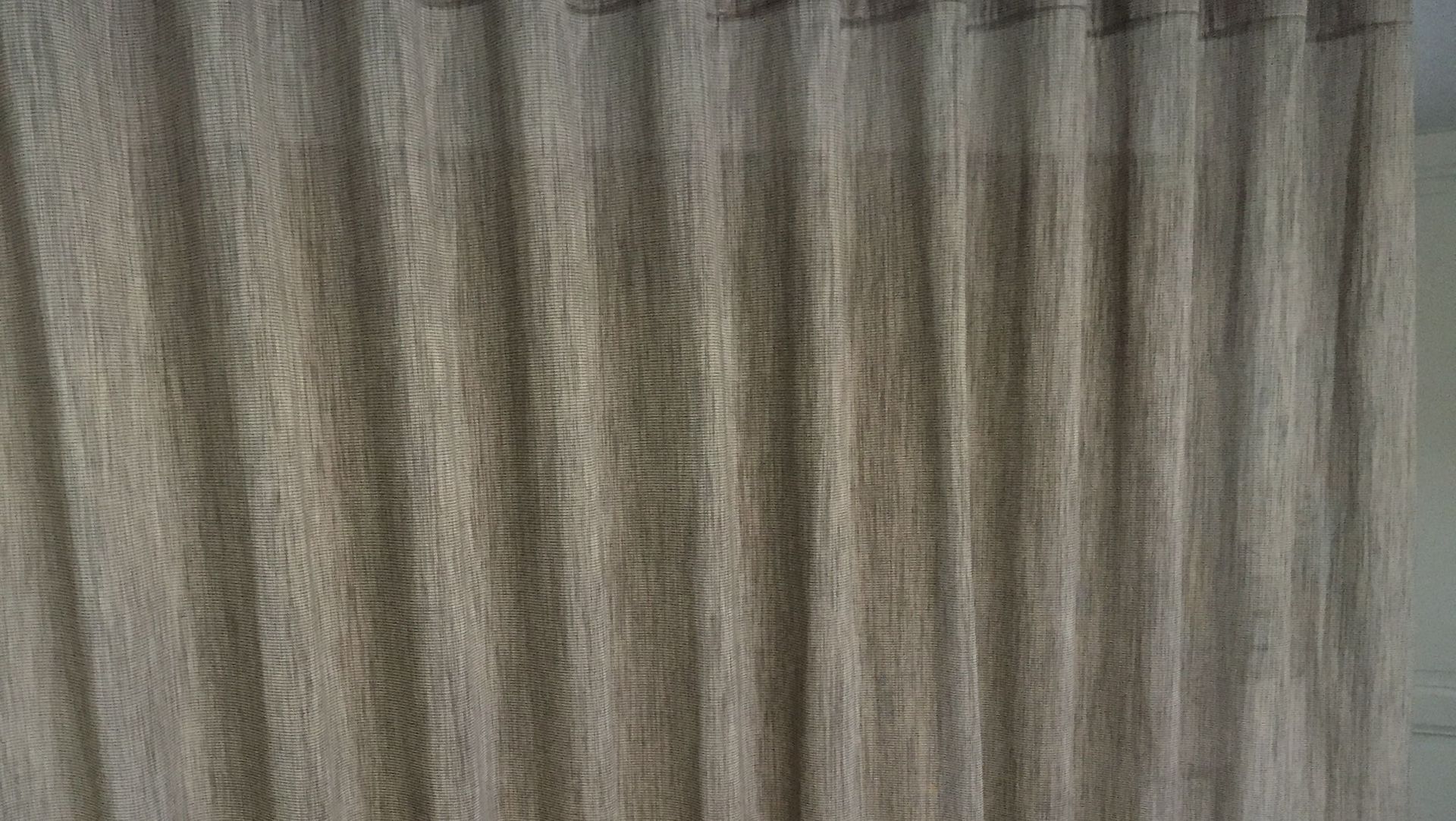 Primo piano di tende lunghe fino al pavimento, di colore marrone chiaro e dalla trama irregolare, con pieghe verticali, appese in una stanza.