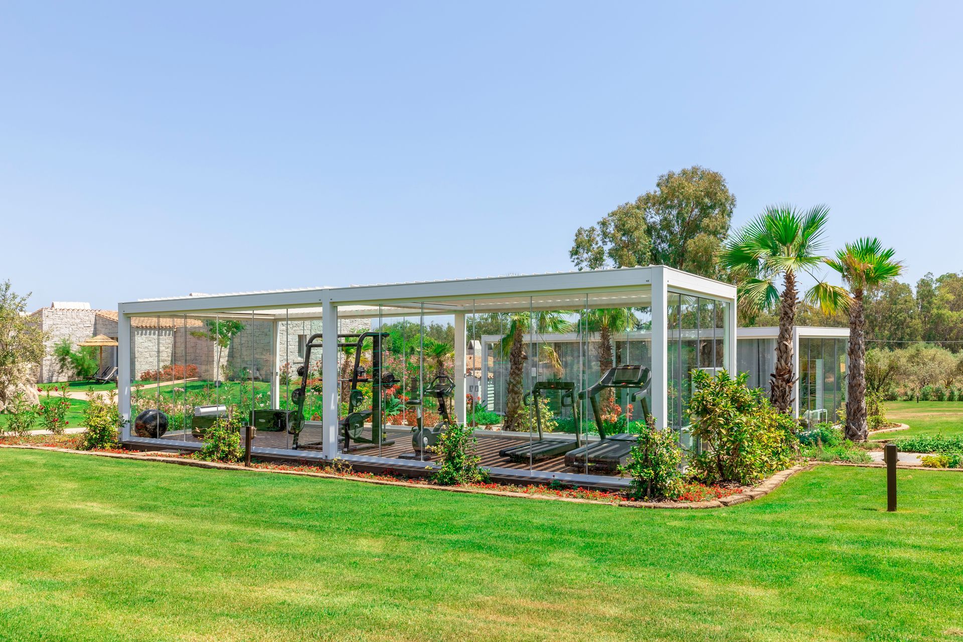 Una palestra a cielo aperto, con struttura bianca e attrezzature per il fitness, situata su un prato sotto un cielo azzurro e limpido.