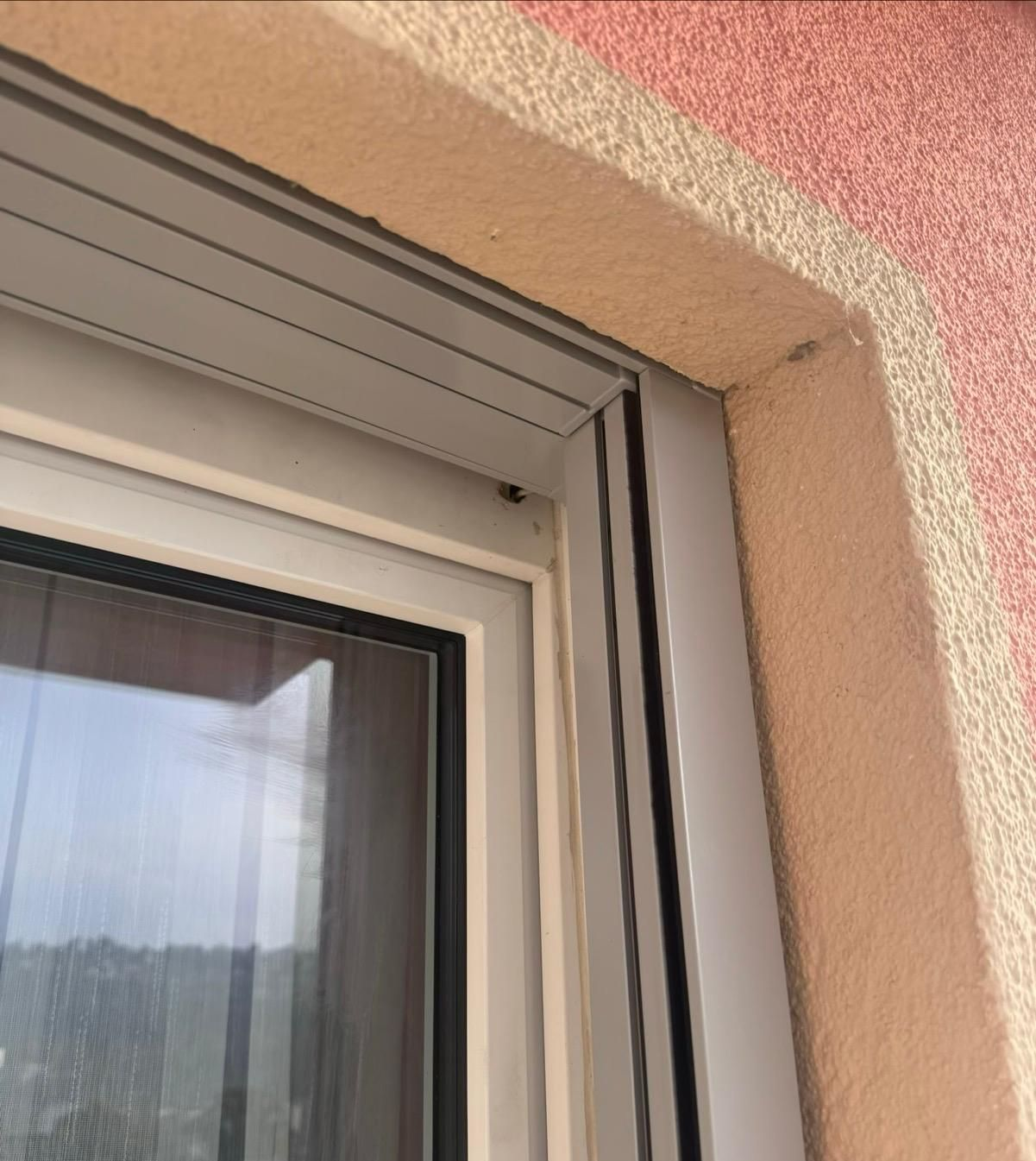 Primo piano dell'angolo superiore destro di un telaio di finestra con binario metallico per tapparella, su una parete con superficie ruvida.