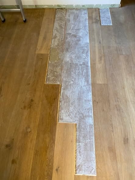 Tavole di parquet di colore chiaro con residui di colla bianca, posate su un pavimento durante una ristrutturazione domestica.