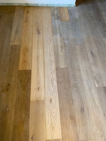 Assi di parquet in legno massello che presentano variazioni di colore, che vanno dal beige chiaro al marrone grigiastro.