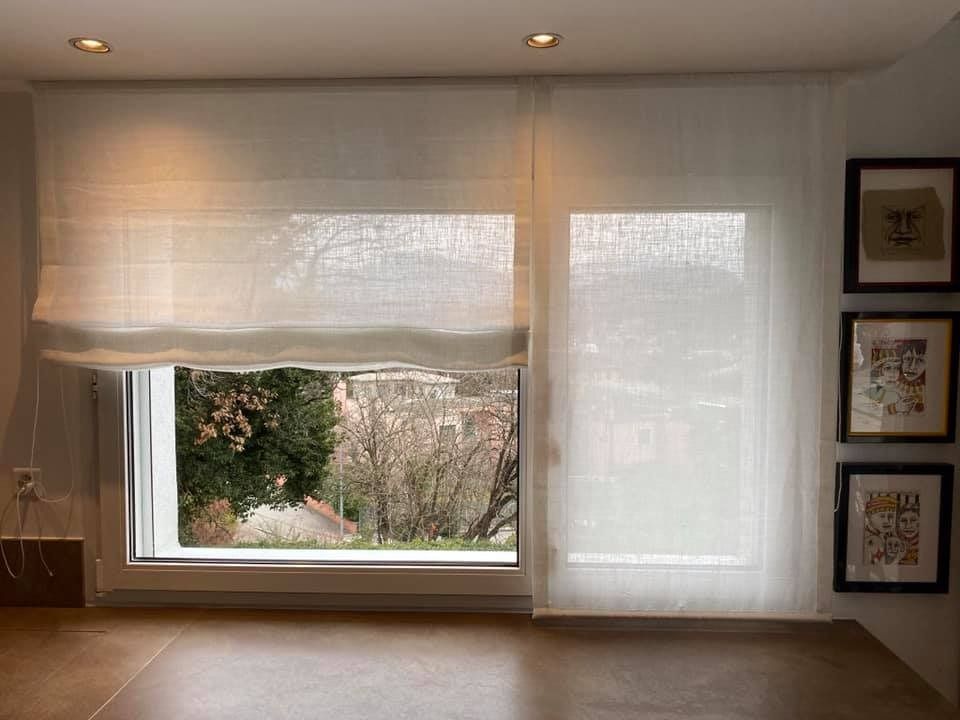 Una stanza luminosa con una finestra dotata di tende a pacchetto bianche trasparenti e tre opere d'arte incorniciate appese alla parete adiacente.