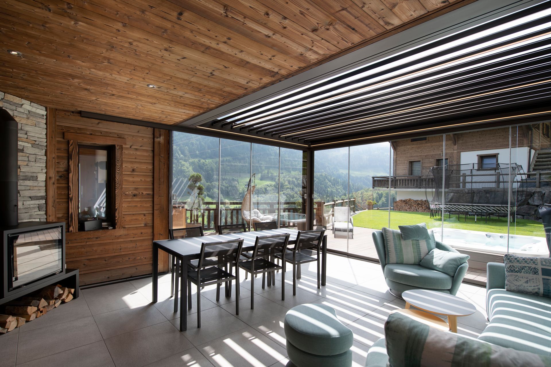 Un patio moderno e a pianta aperta, che si integra perfettamente con l'esterno, con soffitto in legno, tavolo da pranzo, divani e una vista sulle montagne.