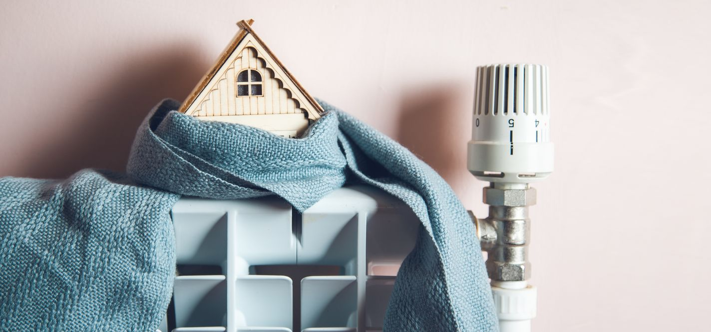 Une écharpe drapée sur une étagère, avec un petit objet de décoration et un robinet de radiateur, contre un mur.