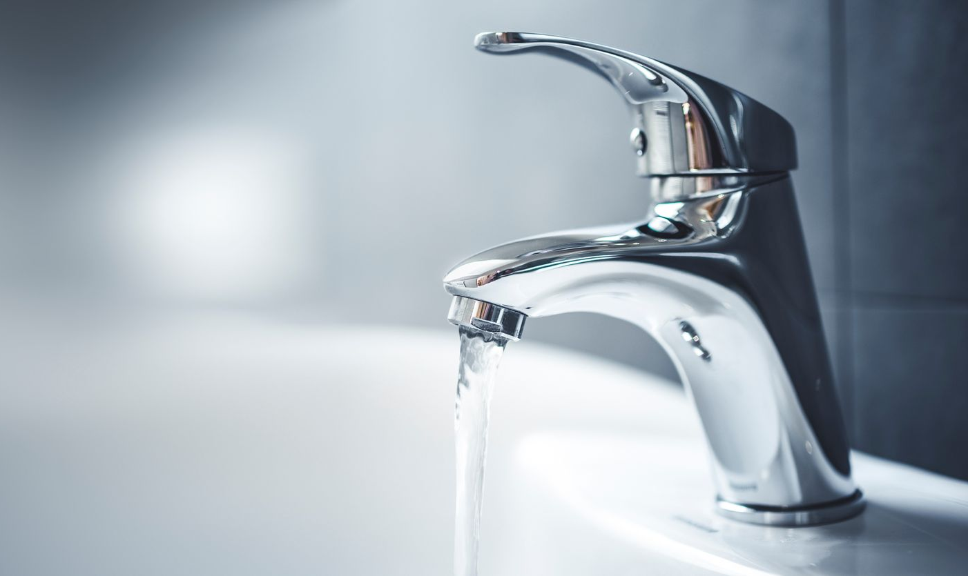 Robinet chromé au-dessus d'un lavabo, avec un fond de salle de bain légèrement flou.