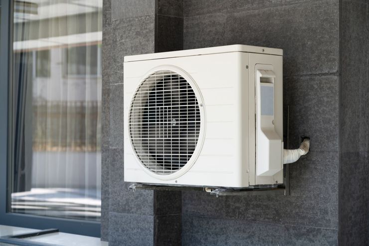 Unité de climatisation extérieure fixée sur un mur à côté d'une fenêtre.
