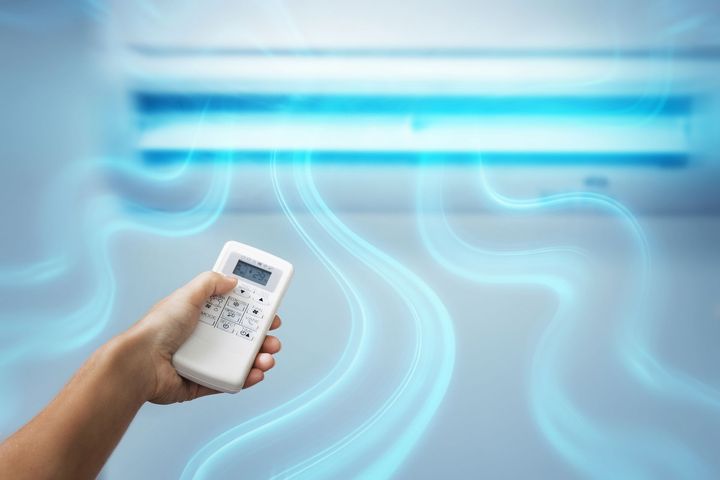 Main tenant une télécommande pointée vers un climatiseur mural avec des lignes de flux d'air.