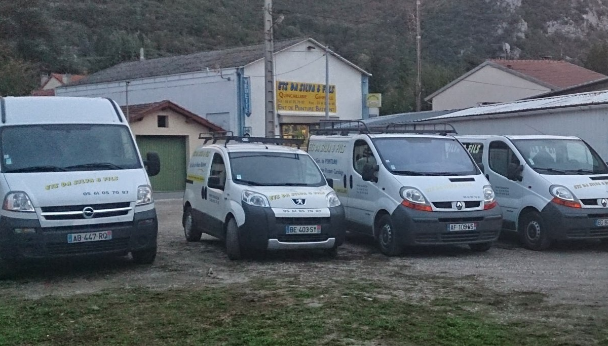 Quatre fourgonnettes blanches garées sur l'herbe près de maisons dans une zone rurale