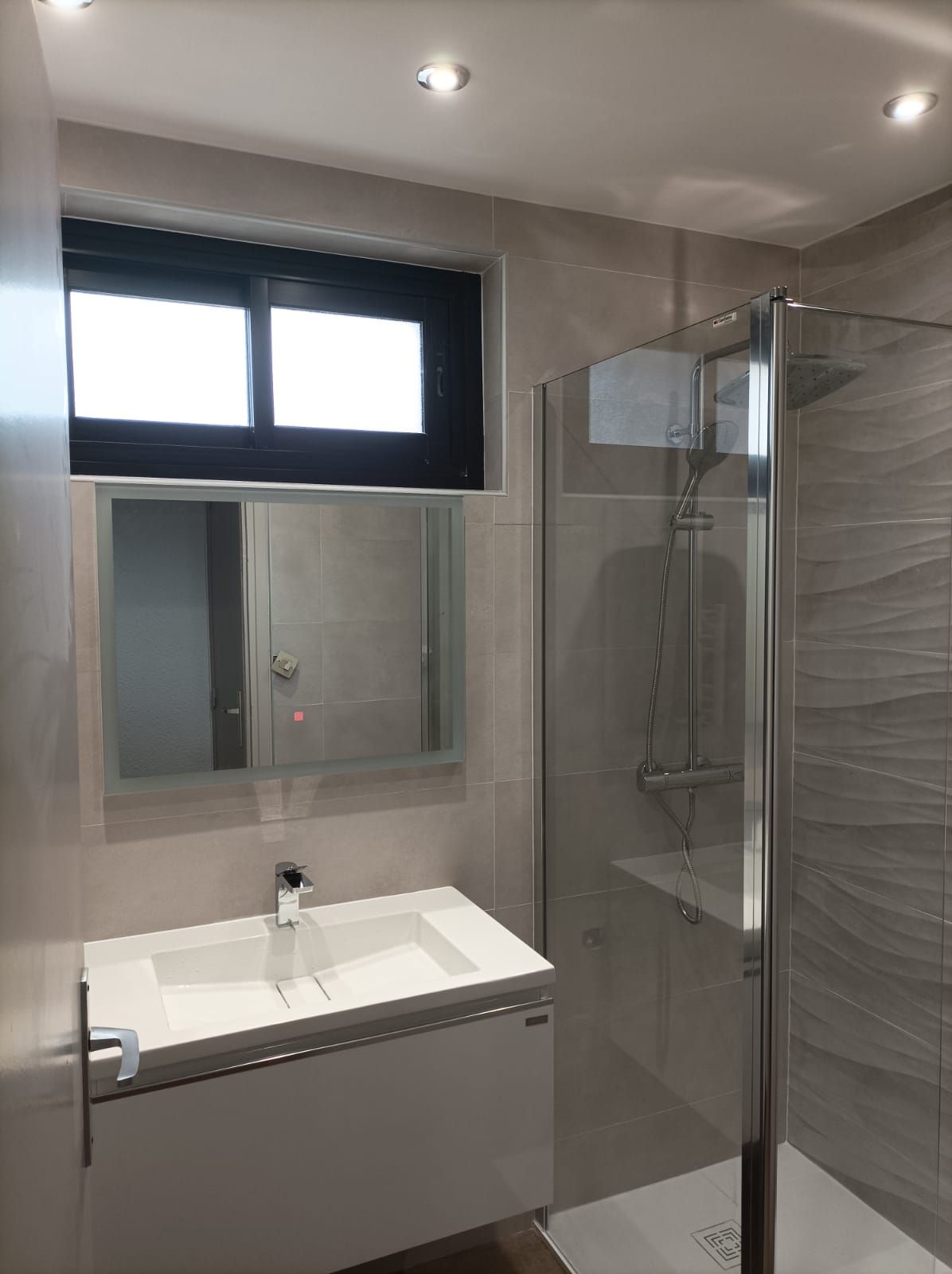 Salle de bains moderne avec lavabo, miroir, fenêtre dépolie et cabine de douche en verre