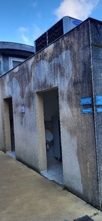 Toilettes publiques en béton avec une porte ouverte et des panneaux bleus sur le mur