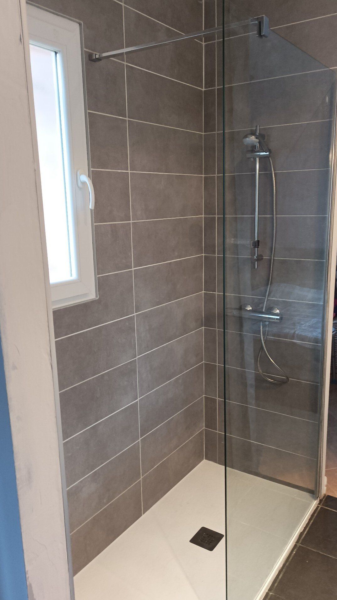 Douche moderne carrelée avec porte en verre, robinetterie chromée et receveur de douche blanc.