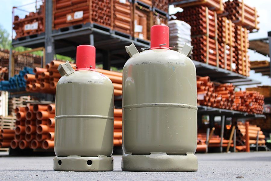 Zwei Gasflaschen stehen vor einem Lager voller Rohre