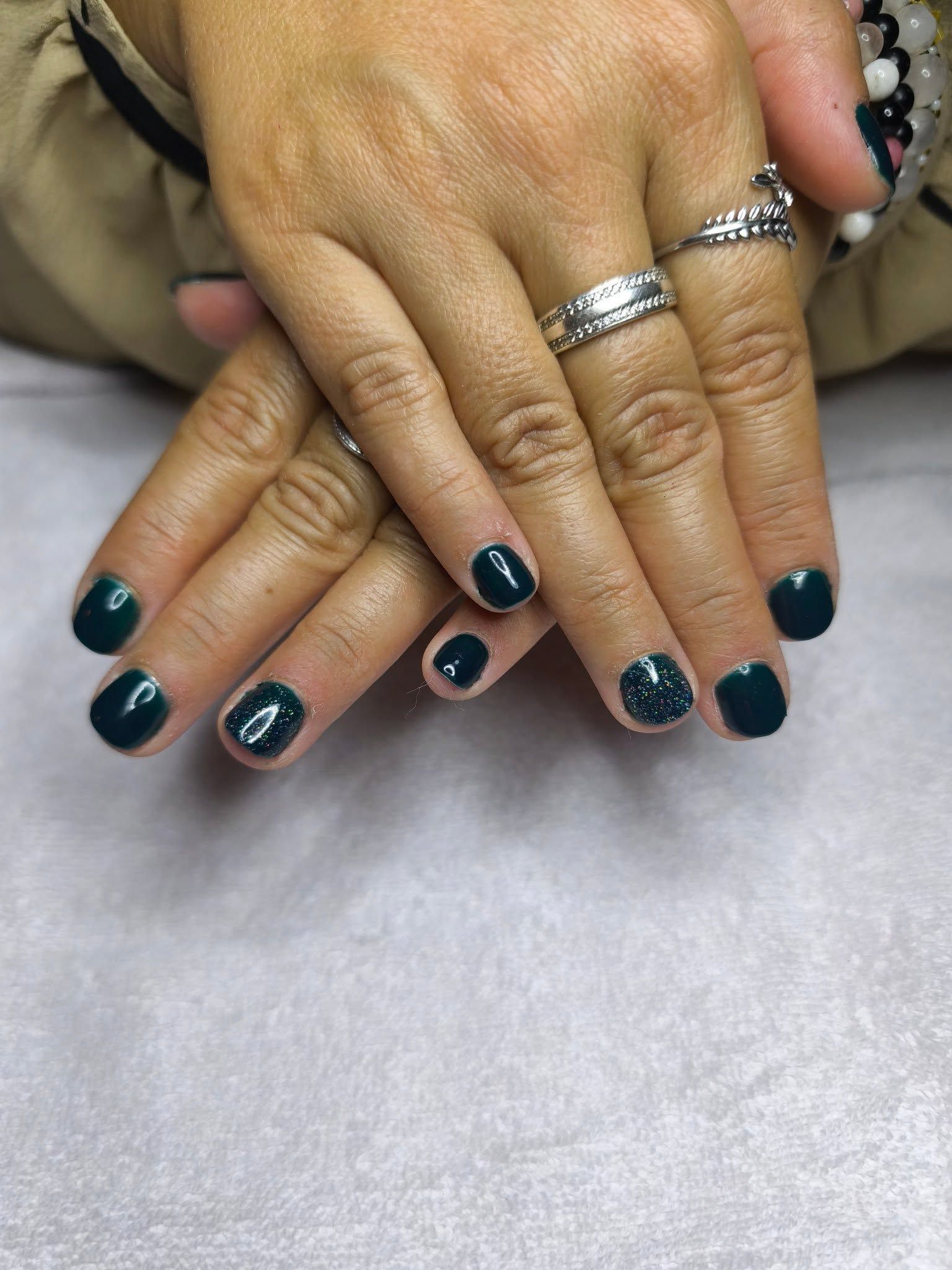 Gros plan sur des mains aux ongles vernis en bleu canard foncé, posées sur une surface blanche.