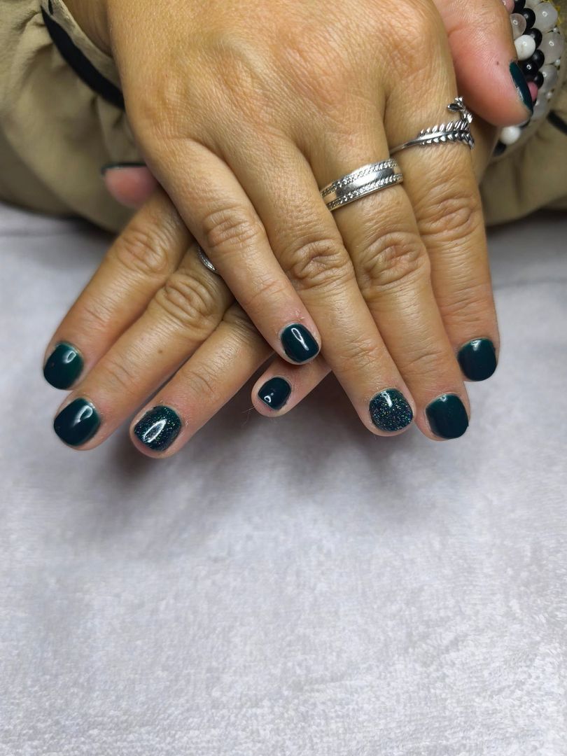 Gros plan sur des mains aux ongles vernis en bleu canard foncé, ornées de bagues argentées, posées sur une surface blanche.