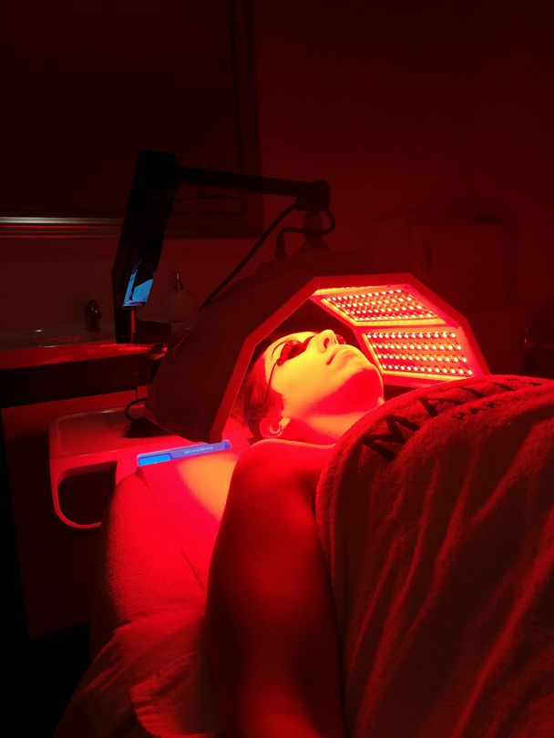 Personne allongée sous un panneau de luminothérapie rouge dans une pièce sombre.