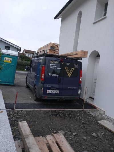 Une camionnette bleue est garée devant une maison blanche.