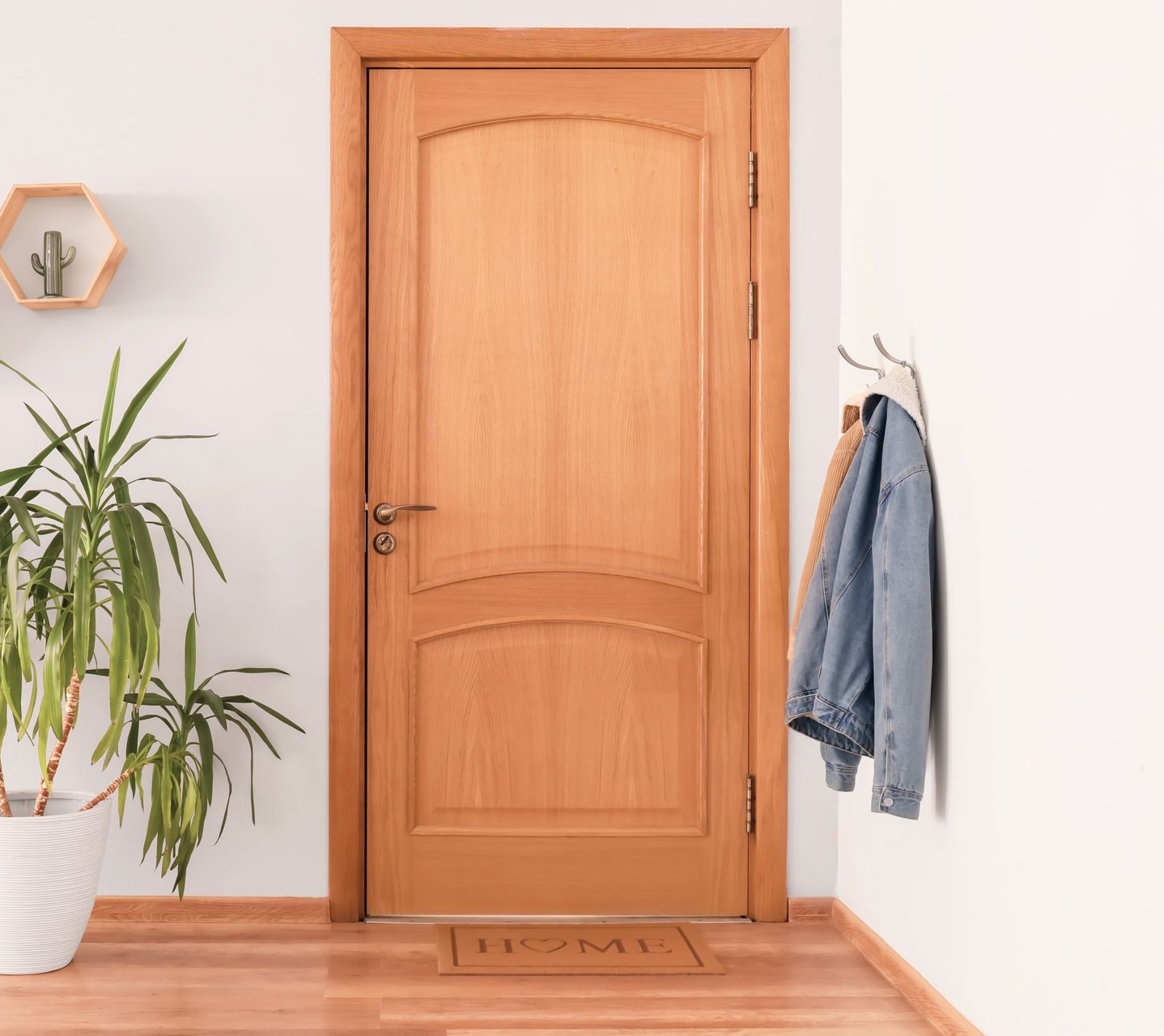 Porte en bois dans un couloir aux murs blancs ; une plante en pot, une étagère et une veste sont accrochées à proximité.