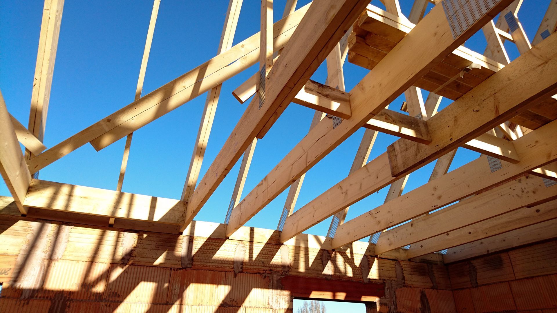 Fermes de toit en bois sur fond de ciel bleu vif, posées sur un bâtiment en briques en construction.