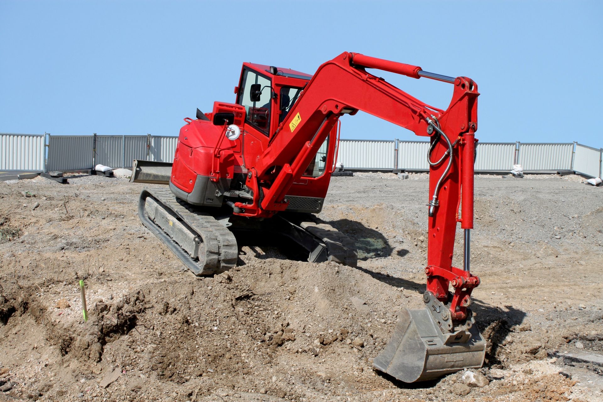 Excavatrice rouge sur une colline de terre, prête à creuser sur un chantier de construction contre un ciel bleu.