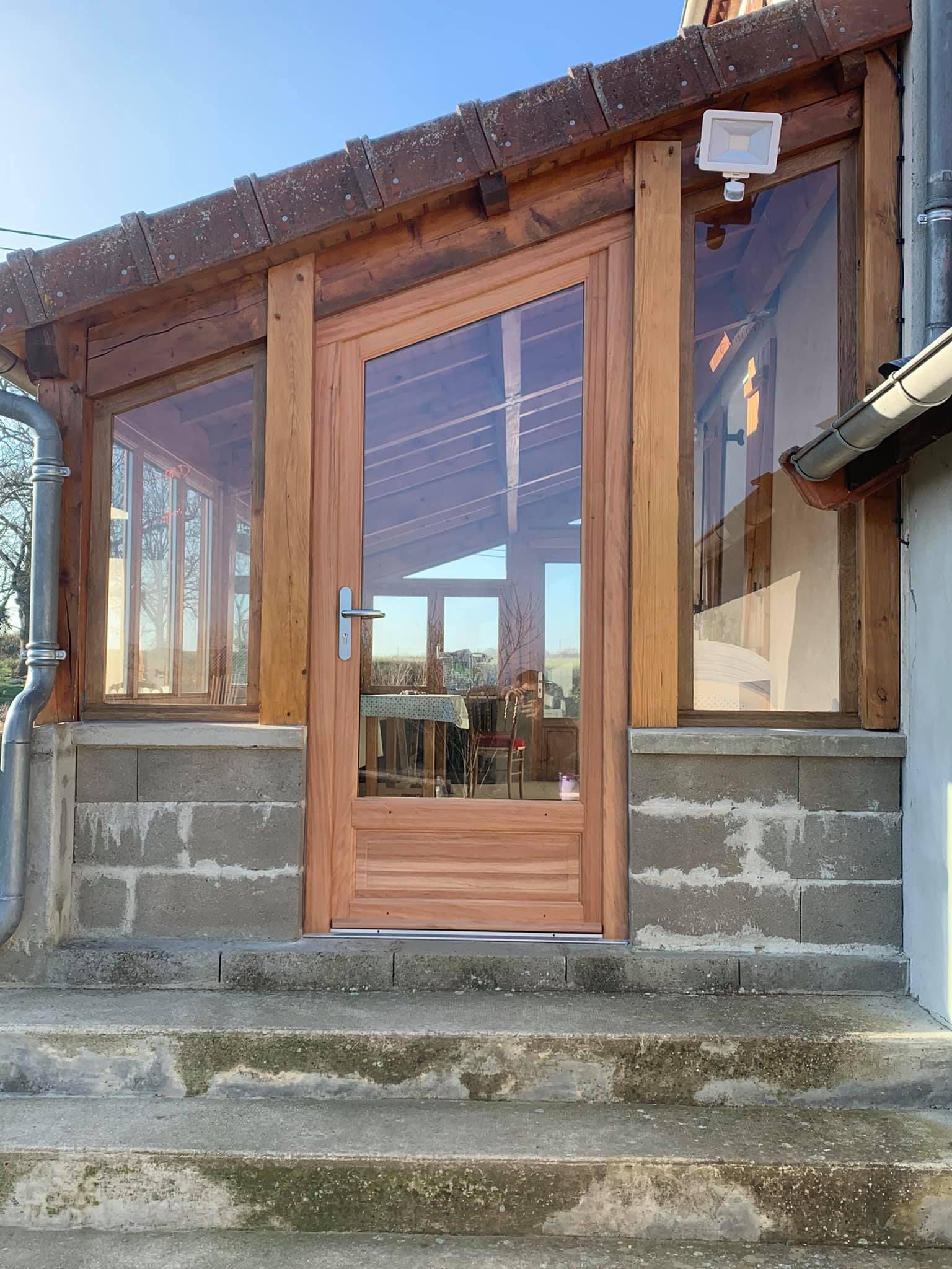 Porte vitrée à cadre en bois avec fenêtres latérales ; entrée du bâtiment avec fondation en brique et marches.