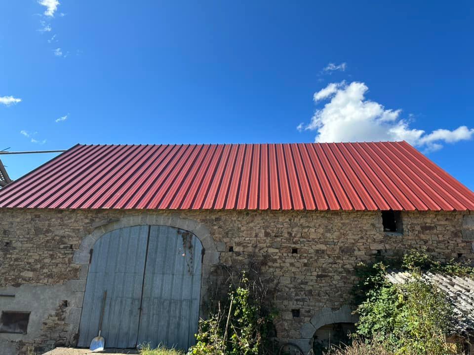 Toit en métal rouge sur une vieille grange en pierre avec un fond de ciel bleu.