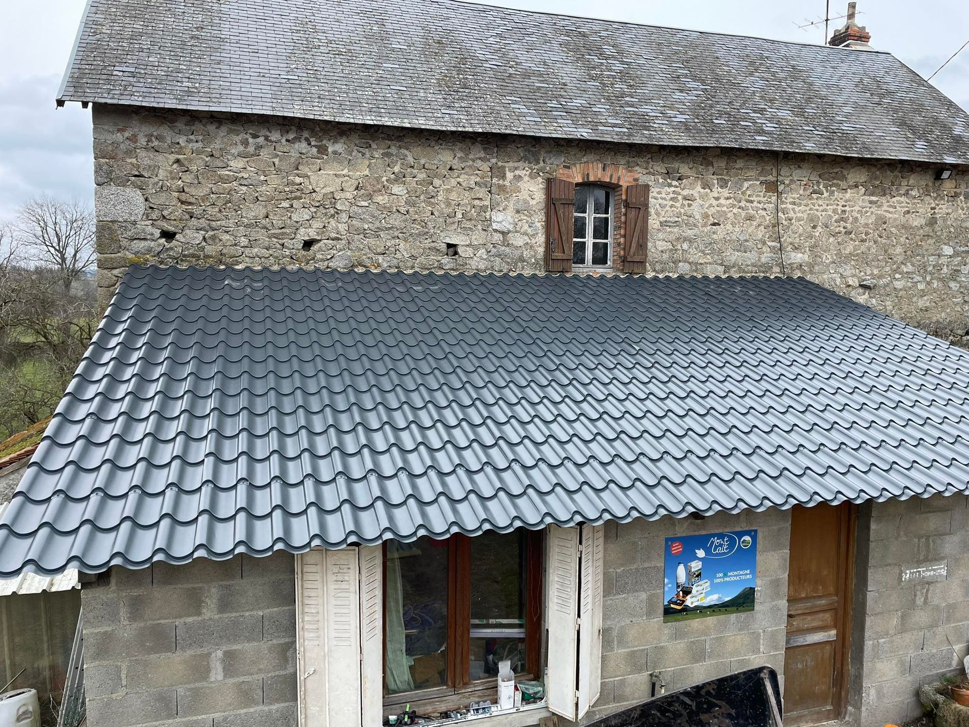 Toiture en tuiles grises d'un petit bâtiment devant un bâtiment en pierre avec un toit en ardoise.