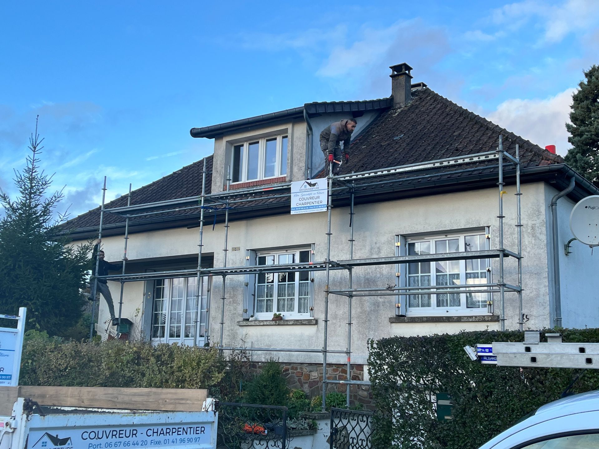 Une maison de plain-pied avec un échafaudage devant et une personne sur le toit.