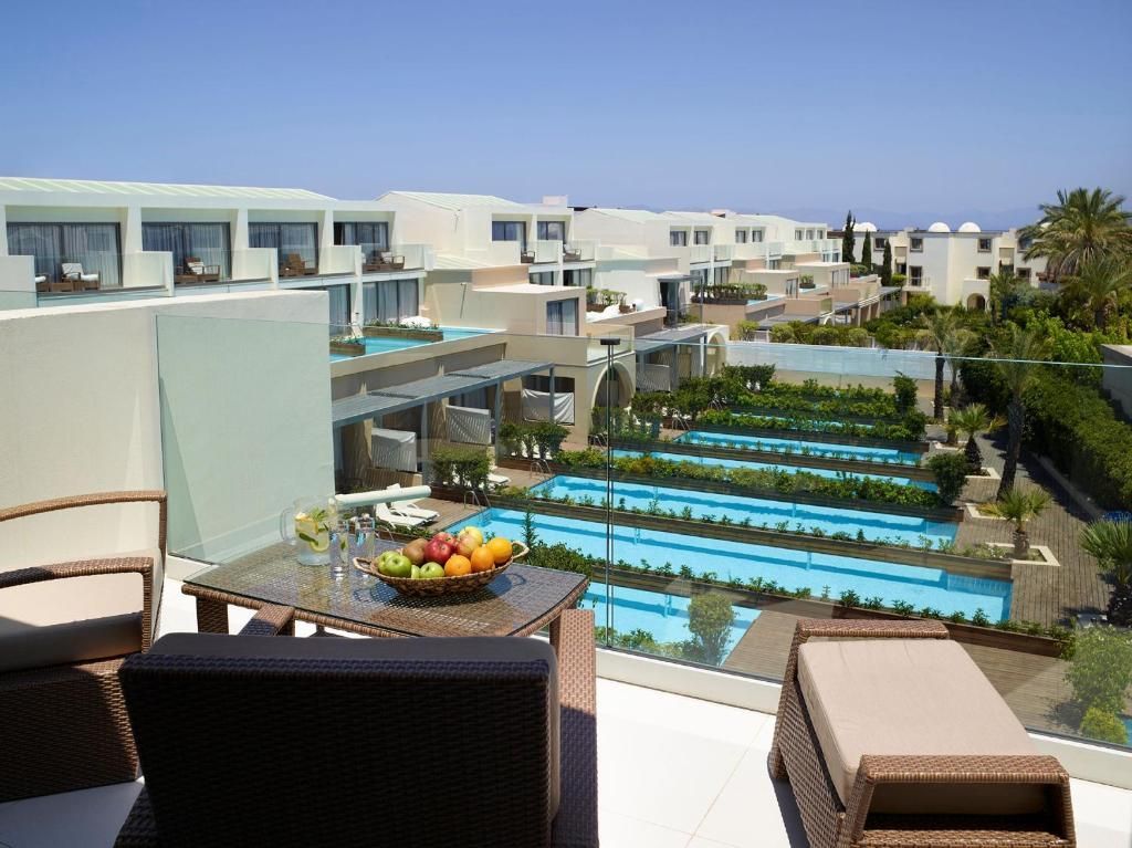 Outdoor hotel view with pools, lounge chairs, and buildings under a bright blue sky.