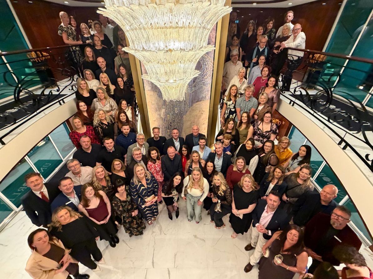 City skyline along a lake at sunset with a tall church steeple, under a vibrant, colorful sky.
