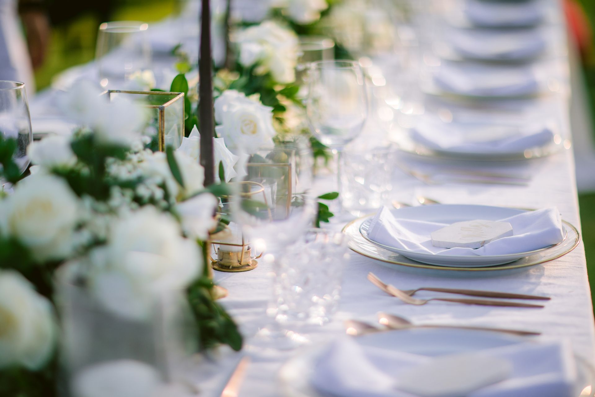 Elegant outdoor table setting with white flowers, candles, and place settings.