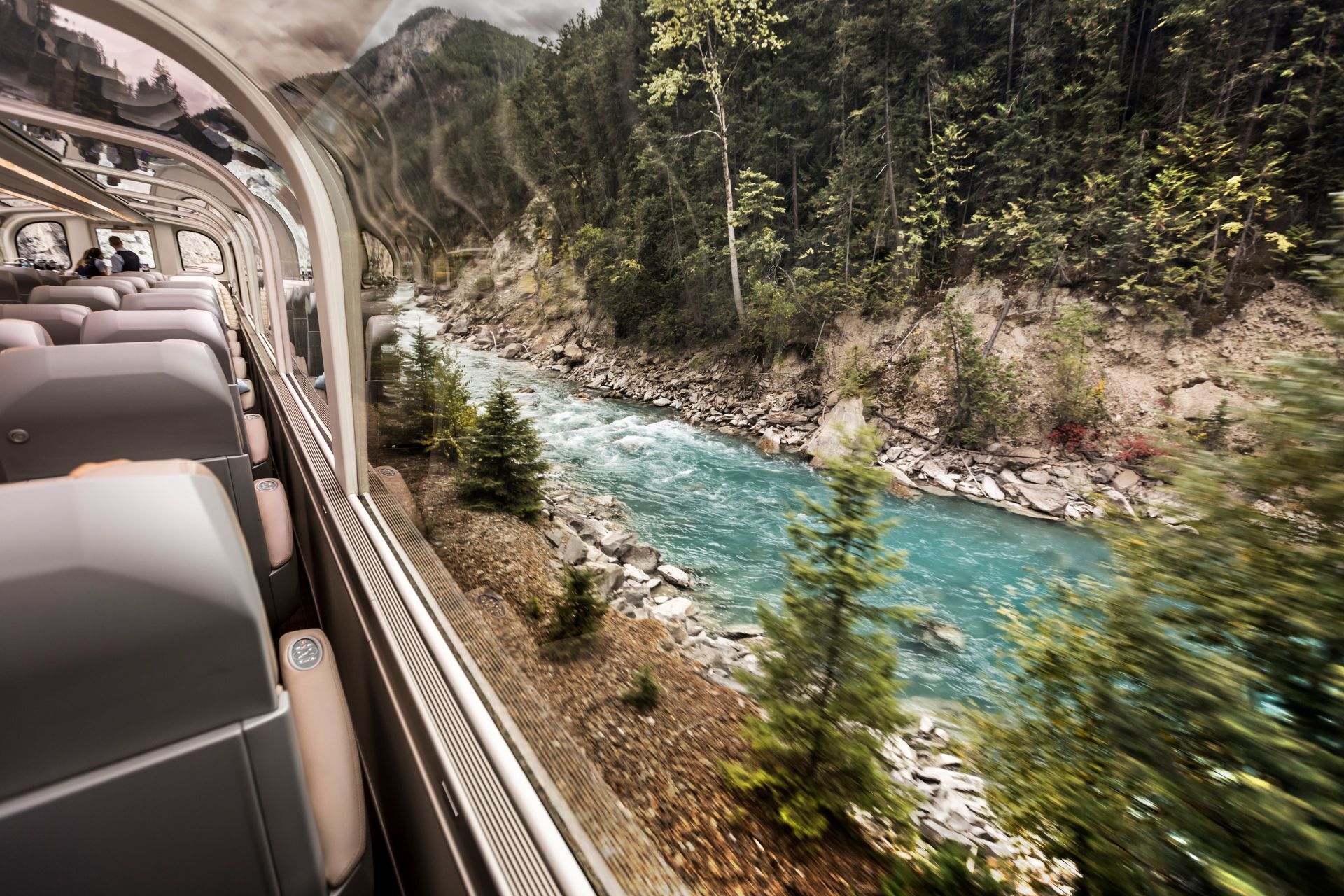 Train interior with view of a turquoise river flowing through a forested canyon.