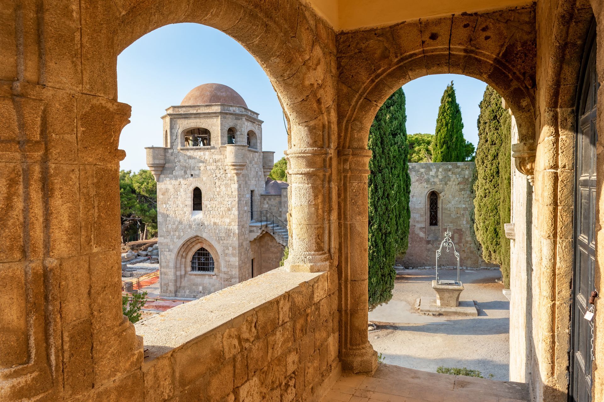 Stone archway framing a view of a castle tower and courtyard with trees.