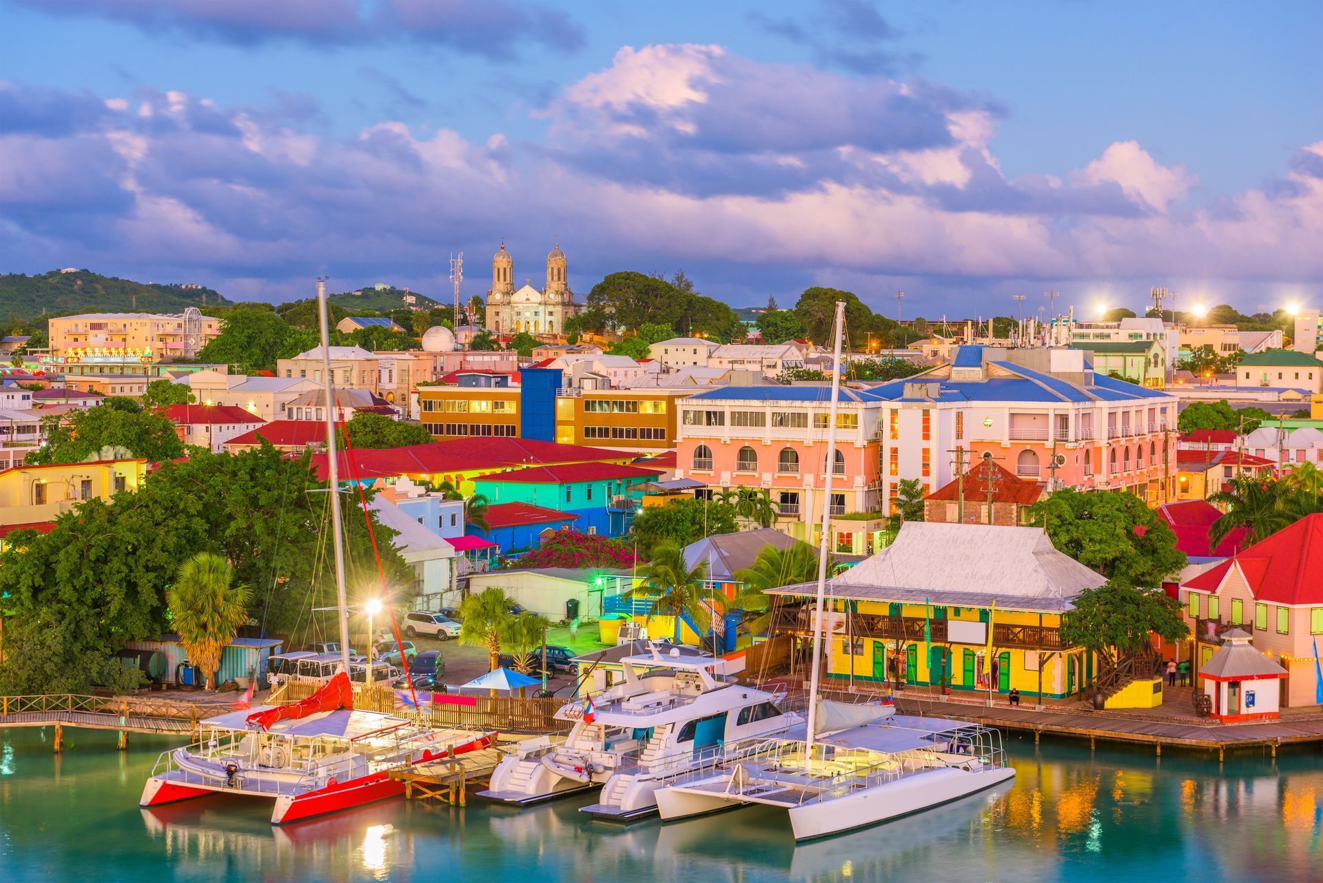 Colorful Caribbean waterfront town with boats docked; buildings with orange, blue, and yellow hues.
