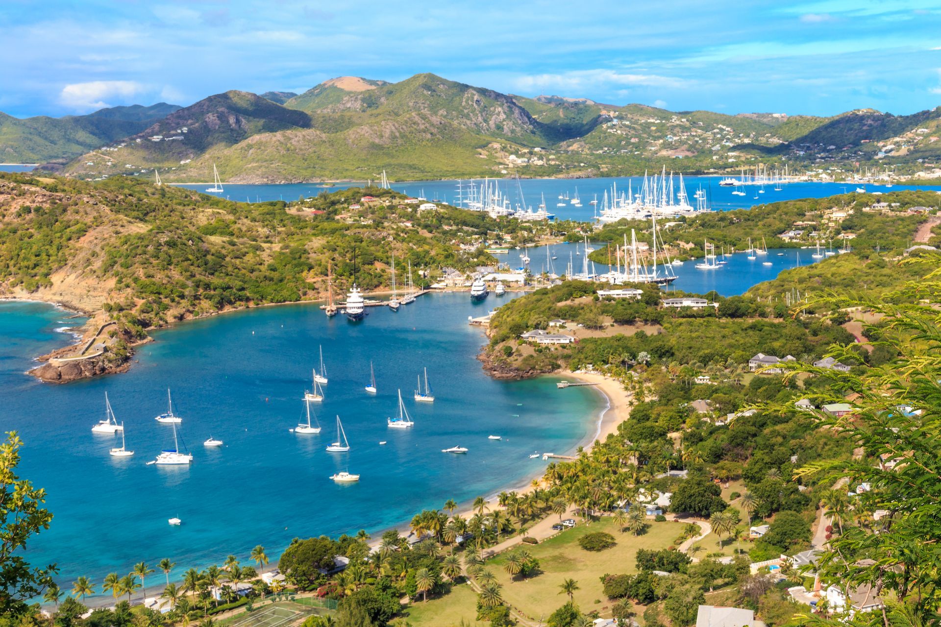 Scenic aerial view of English Harbour, Antigua, with boats in turquoise water surrounded by lush green hills.