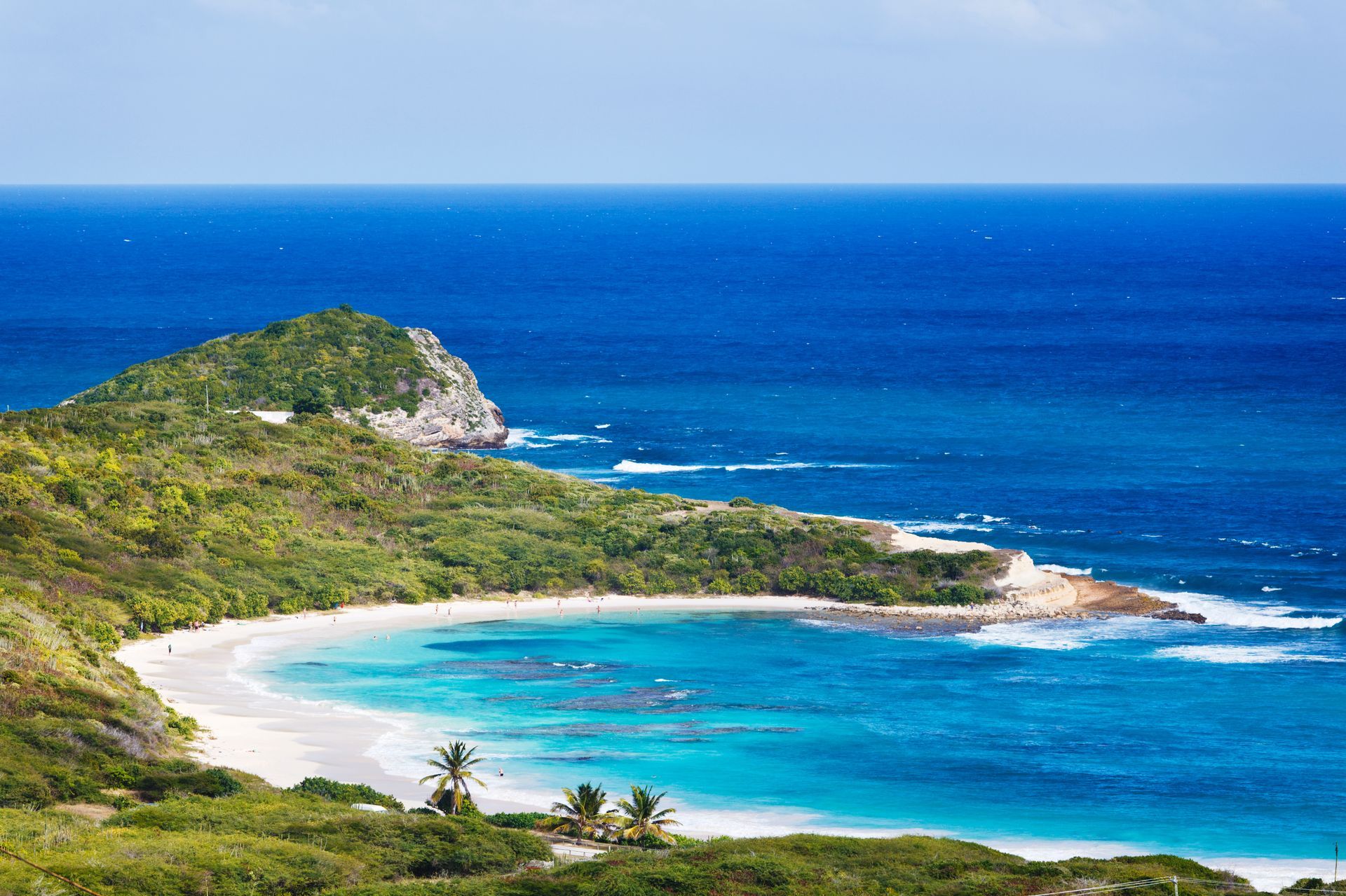 Beach with white sand, turquoise water, and lush green vegetation on a sunny day.