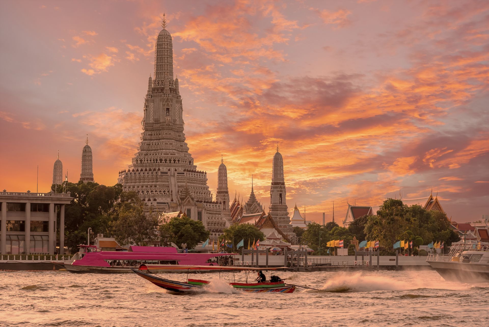 City skyline along a lake at sunset with a tall church steeple, under a vibrant, colorful sky.