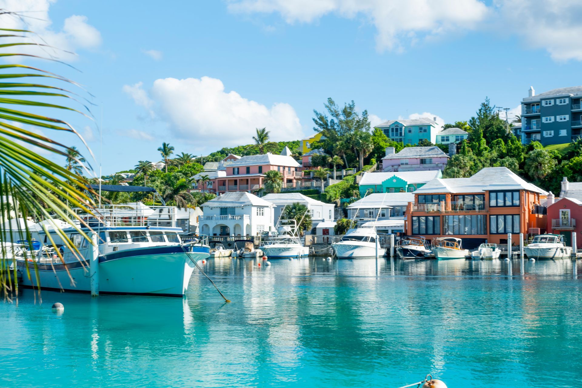Boats docked in turquoise water by colorful houses on a sunny day.