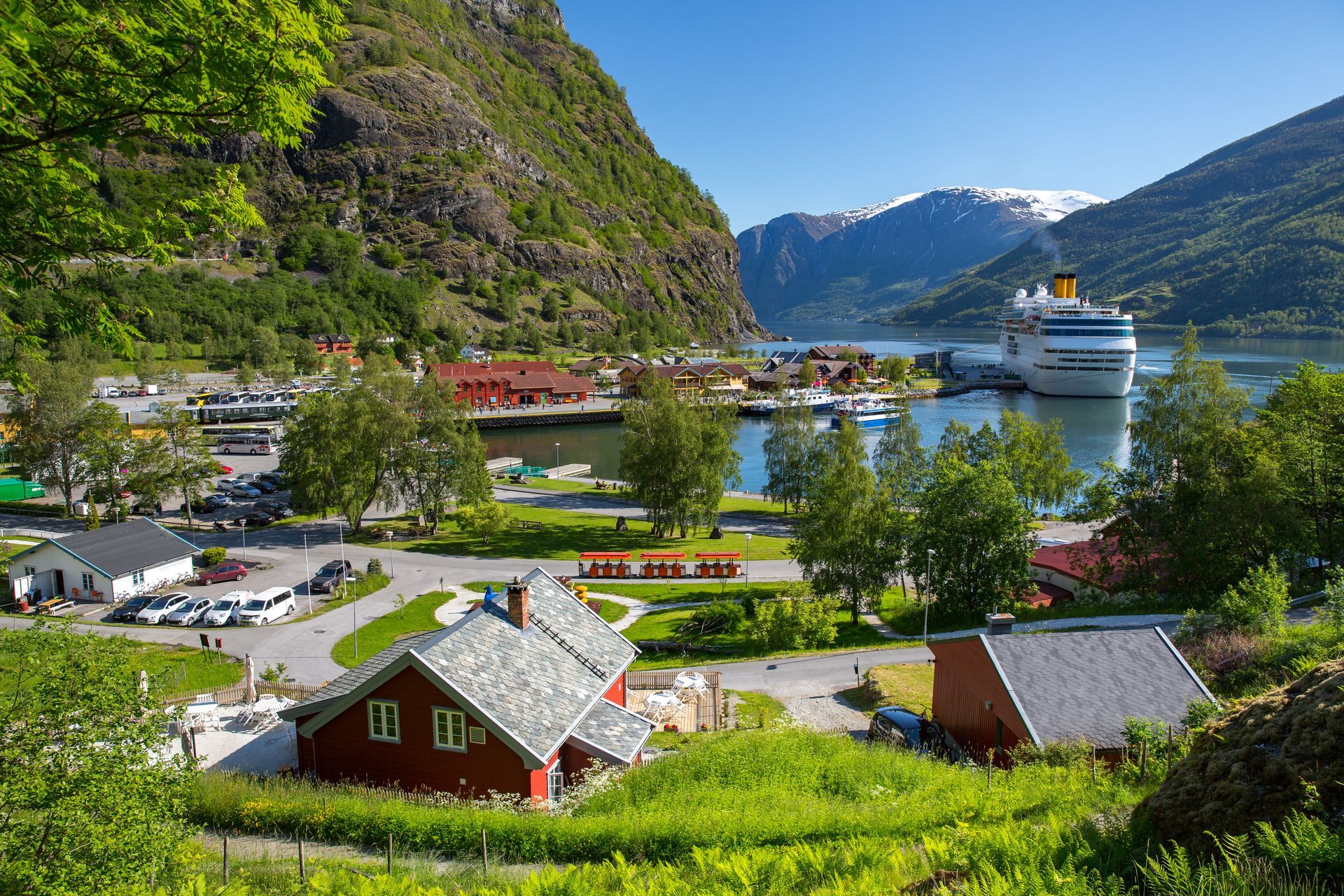Scenic fjord town with red buildings, green hills, and a cruise ship.