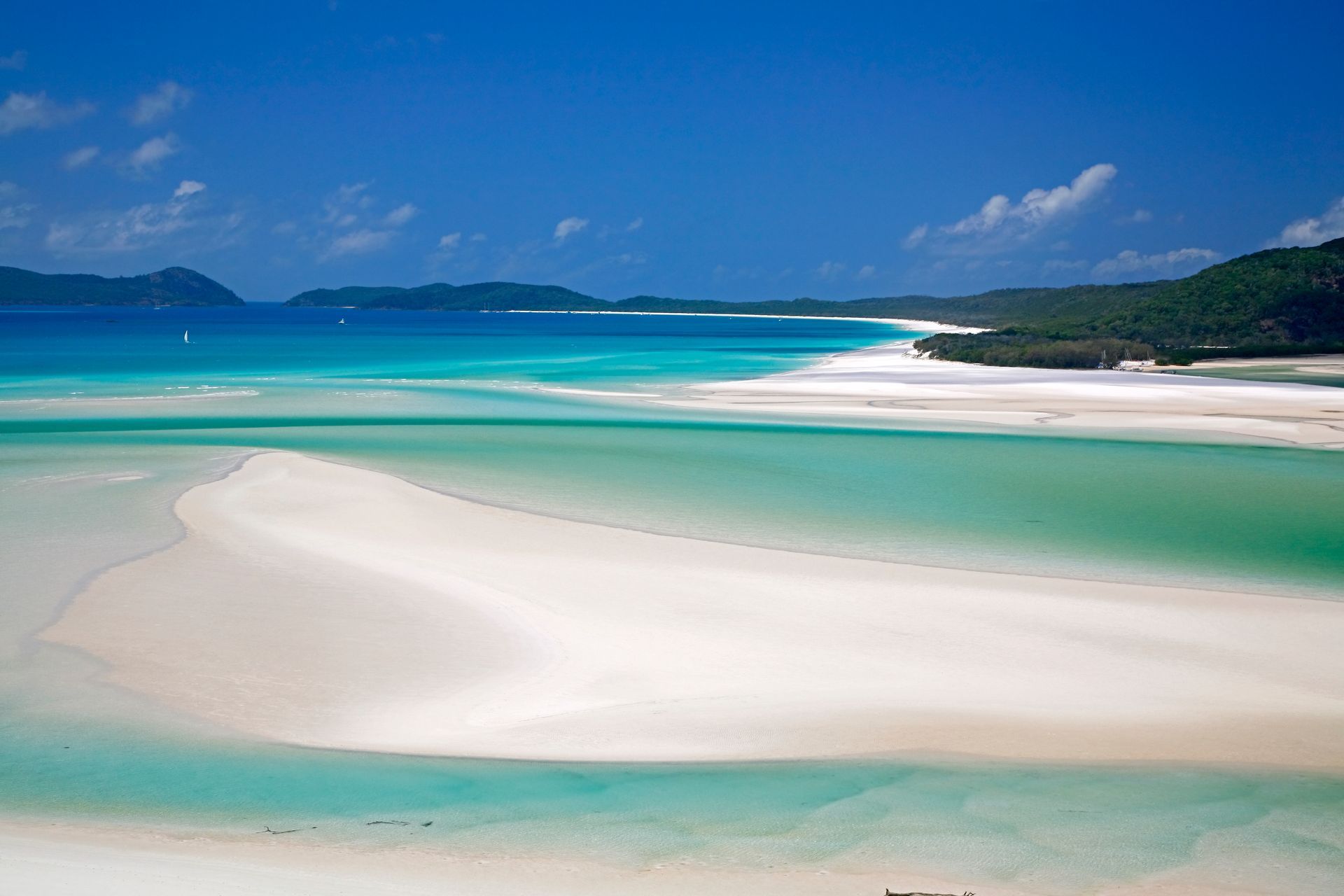 White sand beach with turquoise water under a blue sky; islands in the distance.