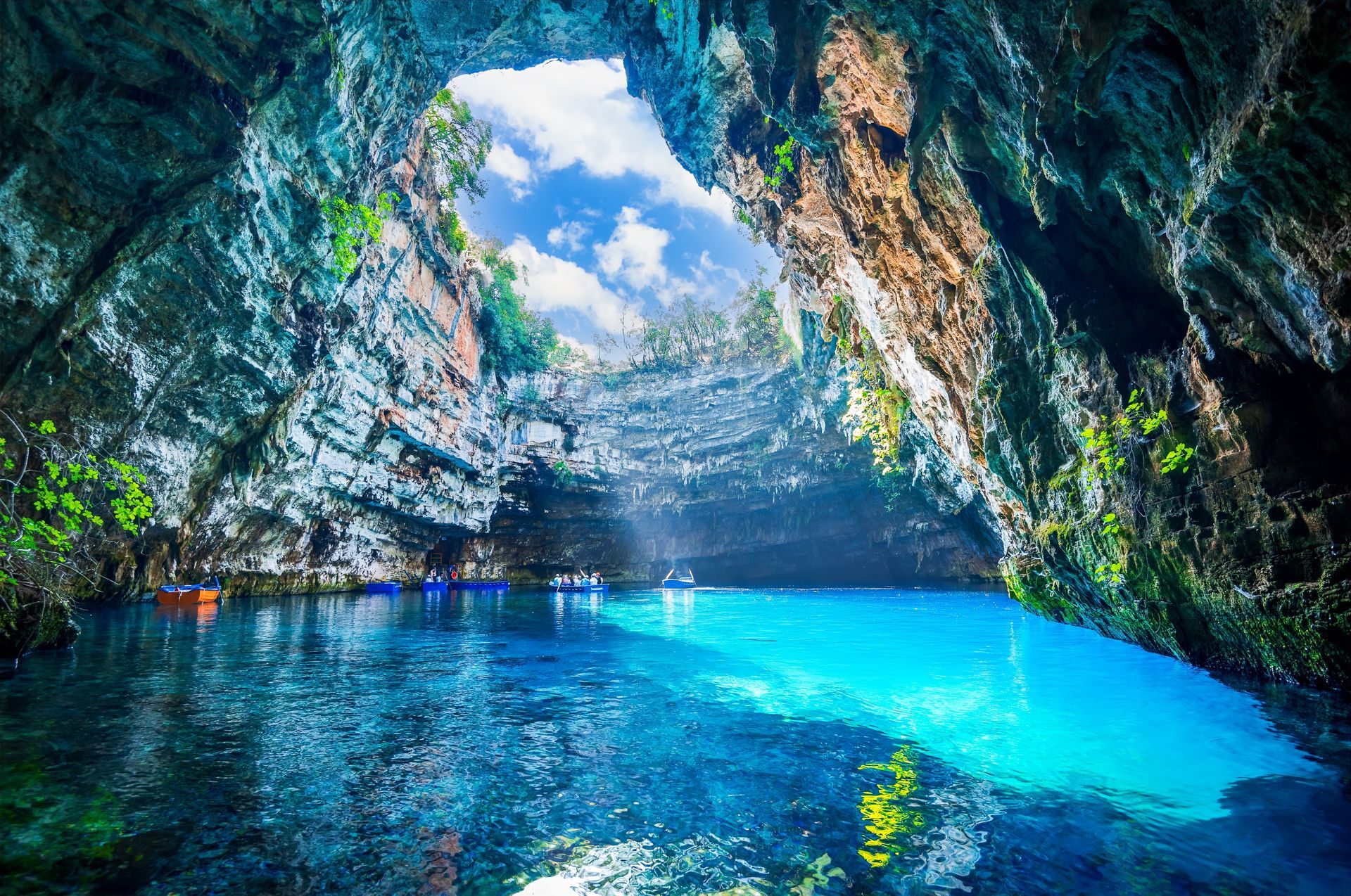 Blue water-filled Melissani Cave in Kefalonia, Greece, with boats and light filtering through the opening.