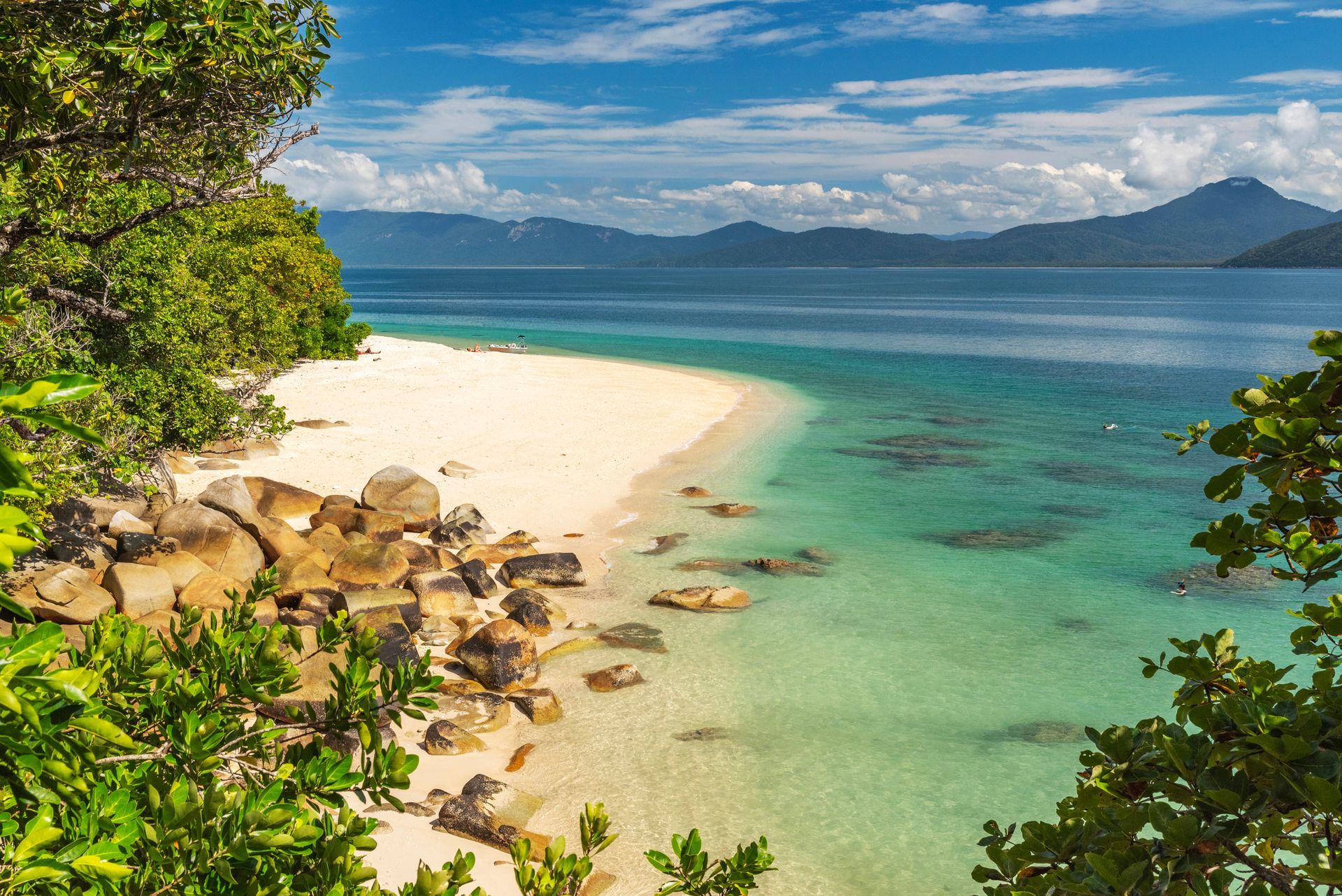 Tropical beach with white sand, turquoise water, and lush green vegetation under a blue sky.