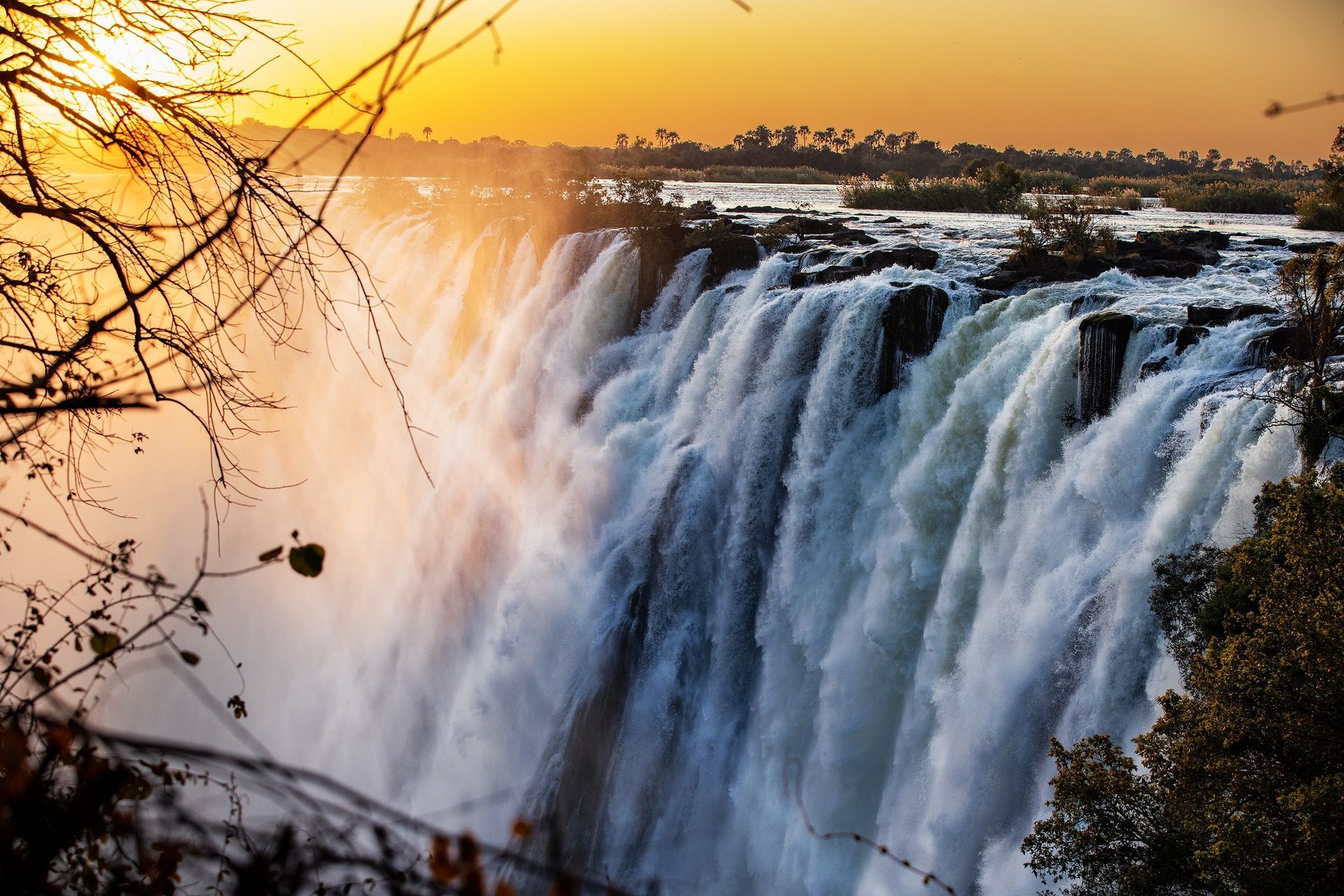 Waterfall cascading over a cliff, with mist rising into a golden sunset.