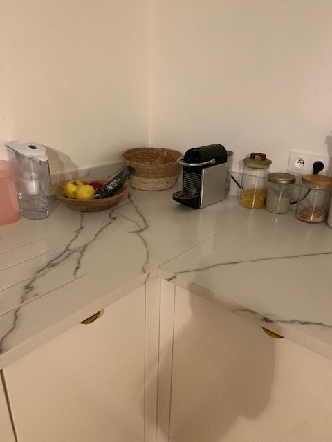 Comptoir de cuisine avec machine à café, corbeille à fruits et contenants. Armoires blanches.