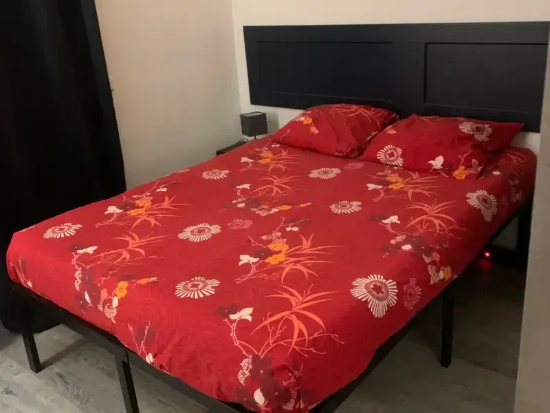 Parure de lit fleurie rouge sur un cadre de lit, avec une tête de lit bleu foncé et des rideaux noirs.