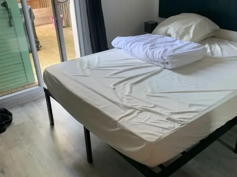 Un lit avec un drap blanc froissé, une couette et un oreiller près d'une porte coulissante en verre.